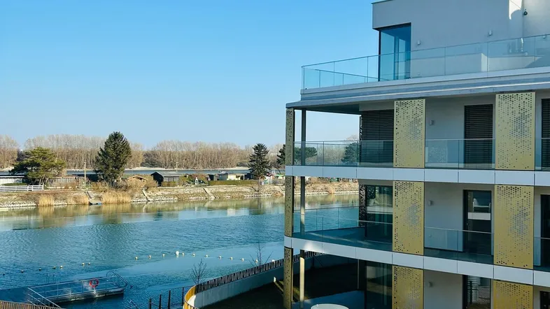 Modernes Gebäude am Wasser mit Balkonen und Blick auf den See.