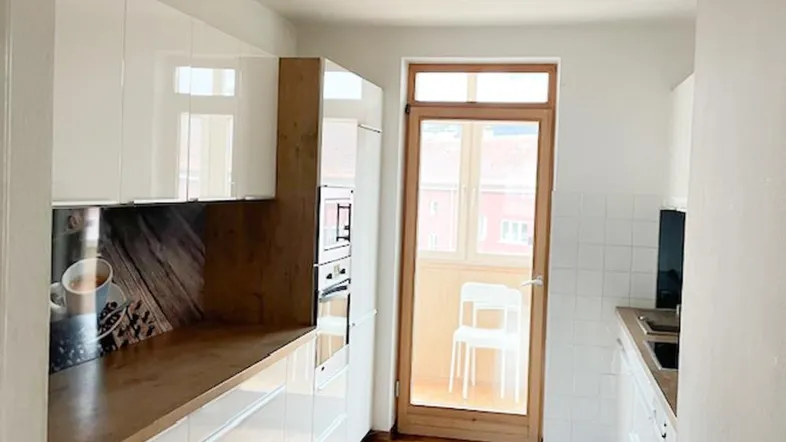 Helle Küche mit weißen Hochglanzfronten, Holzarbeitsplatte und Zugang zum Balkon.