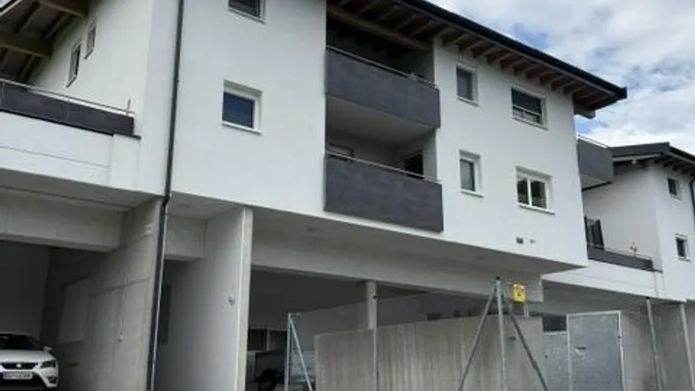 Moderne Wohnanlage mit Balkonen und Zufahrt zur Tiefgarage unter bewölktem Himmel.