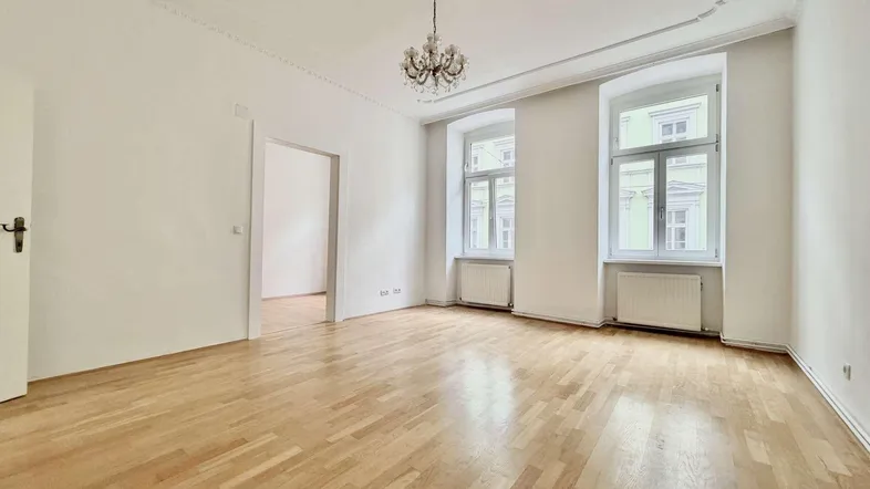Helles Zimmer mit hohen Decken, Stuckverzierungen und Parkettboden, ideal als Wohnzimmer.