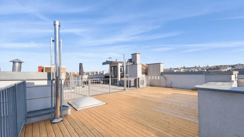 Geräumige Dachterrasse mit Holzboden und weitem Blick über die Stadt unter blauem Himmel.
