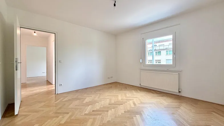Helles Zimmer mit Fischgrätparkett und weiß gestrichenen Wänden, bereit zur individuellen Gestaltung.