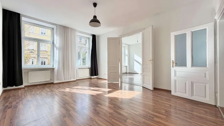 Helles Wohnzimmer mit dunklem Laminatboden, weißen Wänden und Blick auf die Straße.