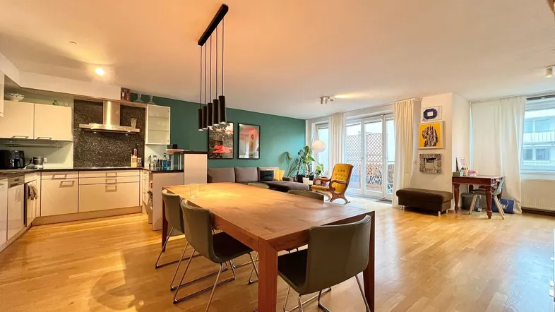 Geräumiger offener Wohn-Essbereich mit moderner Küche, Holzboden und Zugang zum Balkon.