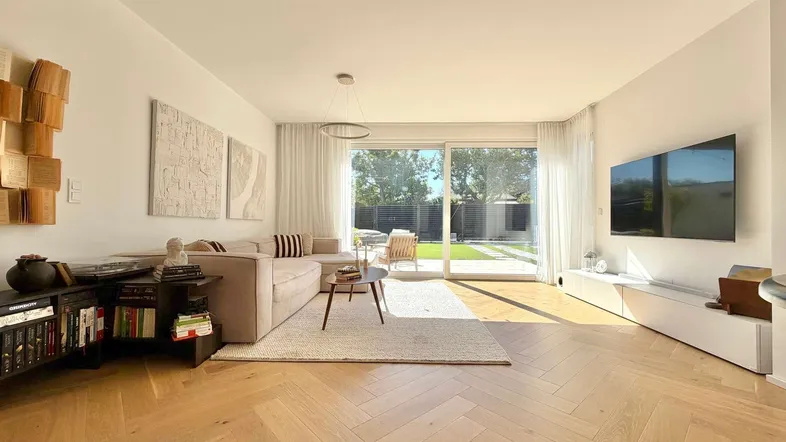 Helles Wohnzimmer mit modernem Sofa, Holzboden und direktem Zugang zum gepflegten Garten.