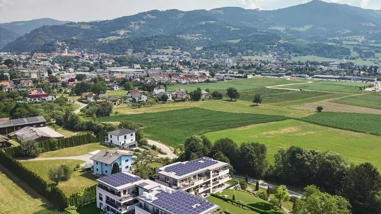 Moderne Wohnanlage mit Solarpaneelen auf den Dächern, eingebettet in eine grüne Landschaft mit Bergblick.