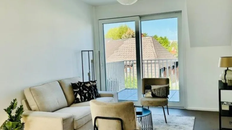 Helles Wohnzimmer mit beigem Sofa, Holzboden und Zugang zu einem Balkon mit Aussicht.