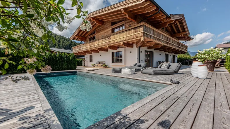 Charmantes Holzchalet mit privatem Pool und großer Holzterrasse, umgeben von grüner Natur und Bergblick.