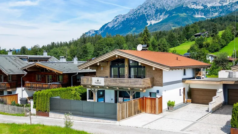 Modernes Haus im alpinen Stil mit Holzbalkonen, weißer Fassade und beeindruckendem Bergblick.