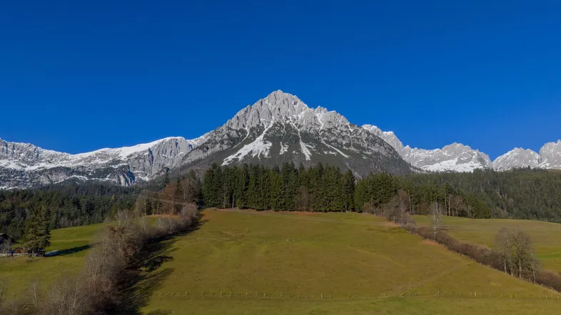 Majestätischer Blick auf schneebedeckte Berge und grüne Hügel unter strahlend blauem Himmel.
