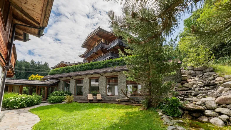 Charmantes Chalet mit gepflegtem Garten, Steinfassade und kleinem Bachlauf in alpiner Umgebung.