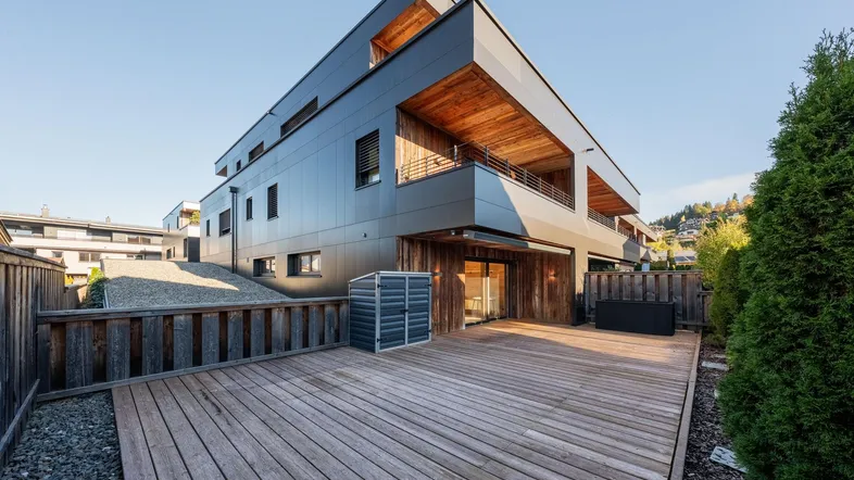 Moderne Architektur mit dunkler Fassade und Holzverkleidung, ergänzt durch eine geräumige Holzterrasse im Freien.