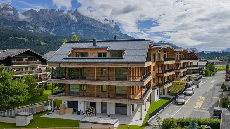 Modernes Mehrfamilienhaus in Holzbauweise mit Balkonen und Bergblick, umgeben von Grünflächen.