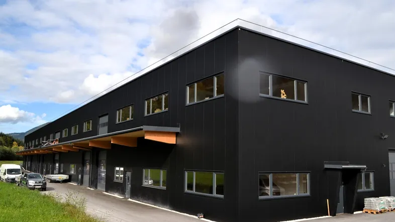 Modernes Geschäftsgebäude mit schwarzer Fassade, großen Fenstern und Holzelementen unter einem Vordach.