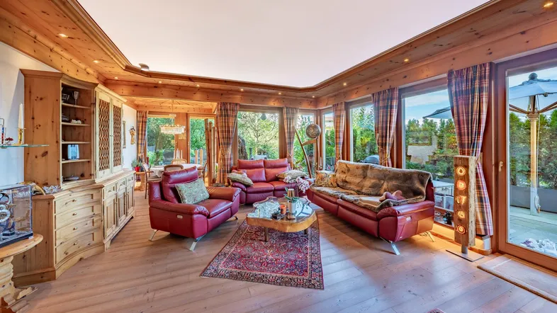 Gemütliches Wohnzimmer mit viel Holz, roten Ledersofas und großen Fenstern, die viel Licht hereinlassen.