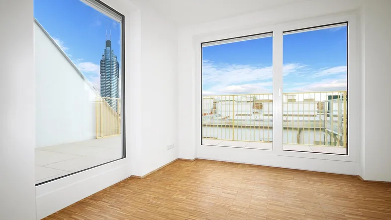 Heller Raum mit Holzboden und großen Fenstern, die einen Blick auf die Stadt bieten.