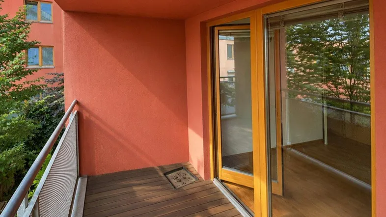 Heller Balkon mit Holzplankenboden, orangefarbenen Wänden und Blick ins Grüne.