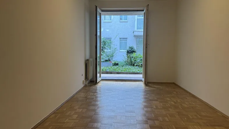 Heller Wohnraum mit Parkettboden und direktem Zugang zu einem begrünten Außenbereich.