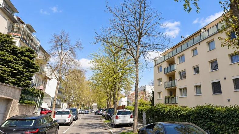 Eine ruhige Wohnstraße mit geparkten Autos und modernen Apartmentgebäuden unter blauem Himmel.