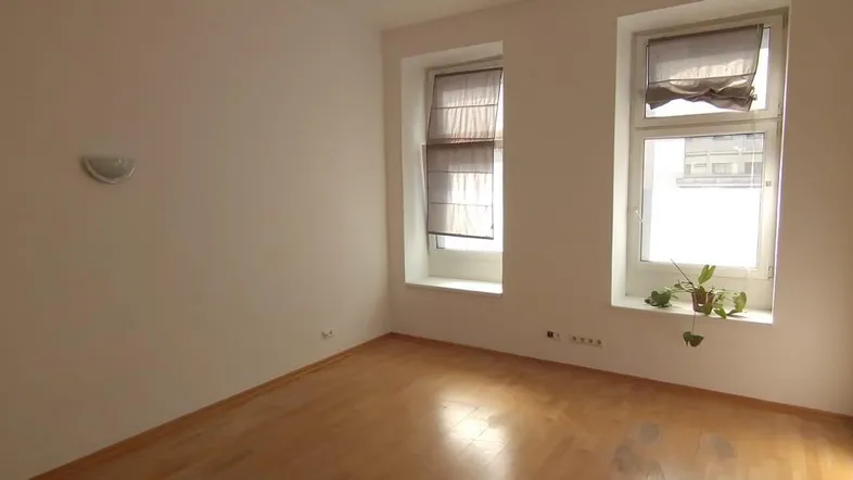 Helles, leeres Zimmer mit Holzboden und zwei Fenstern, bereit zur individuellen Gestaltung.