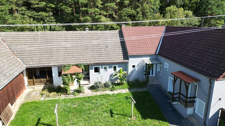 Luftaufnahme des Anwesens mit Wohnhaus, Innenhof und angrenzendem Wald unter blauem Himmel.