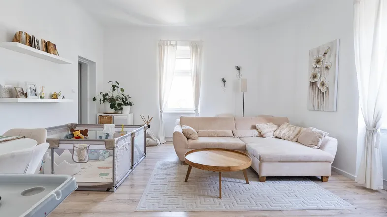 Helles Wohnzimmer mit beigem Ecksofa, Holzboden und einem Spielbereich für Kinder.