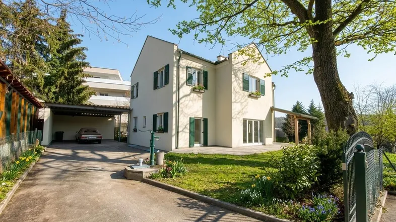 Vorderansicht des Hauses mit gepflegtem Vorgarten, Carport und Zufahrt an einem sonnigen Tag.