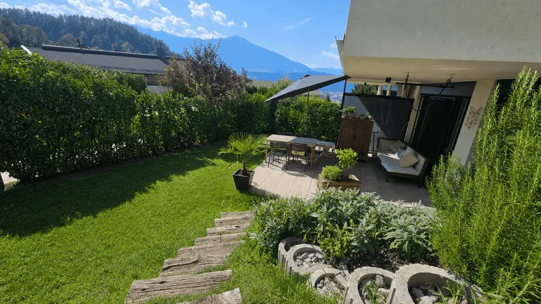 Gepflegter Gartenbereich mit sonniger Terrasse, Sitzgelegenheiten und Blick auf die umliegende Berglandschaft.