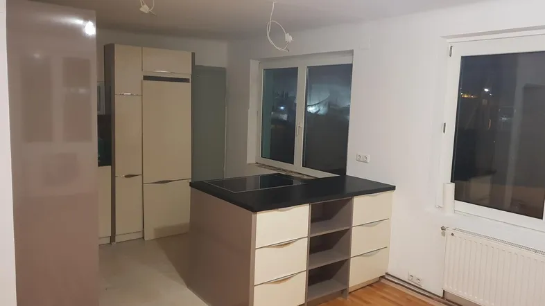 Helle Küche mit Kücheninsel, integrierten Schränken und Holzboden, bereit für die Fertigstellung.