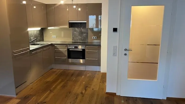 Moderne Küche mit glänzenden Schränken, integrierten Geräten und hellem Holzfußboden.
