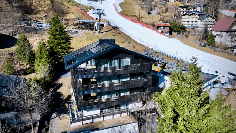 Modernes Gebäude mit Solarpaneelen auf dem Dach, umgeben von einer Skipiste und alpiner Landschaft.