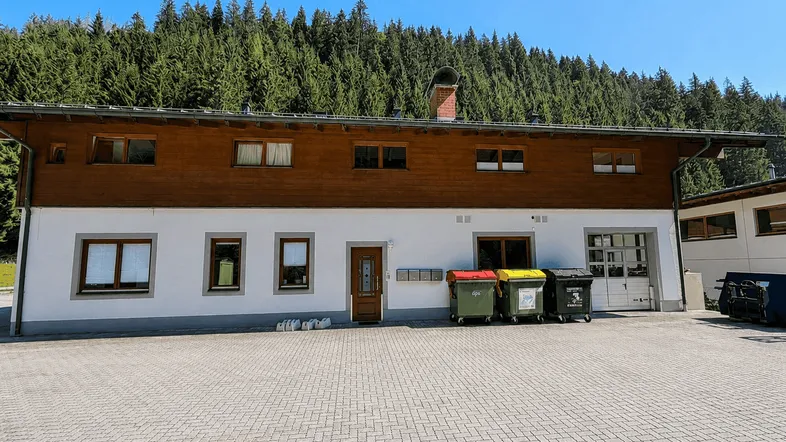 Gebäude mit weißer Fassade, Holzverkleidung und Blick auf den bewaldeten Berg.