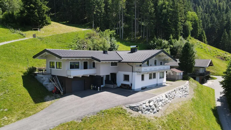 Wohnhaus in sonniger Hanglage mit Blick auf die umliegende Berglandschaft und Wälder.