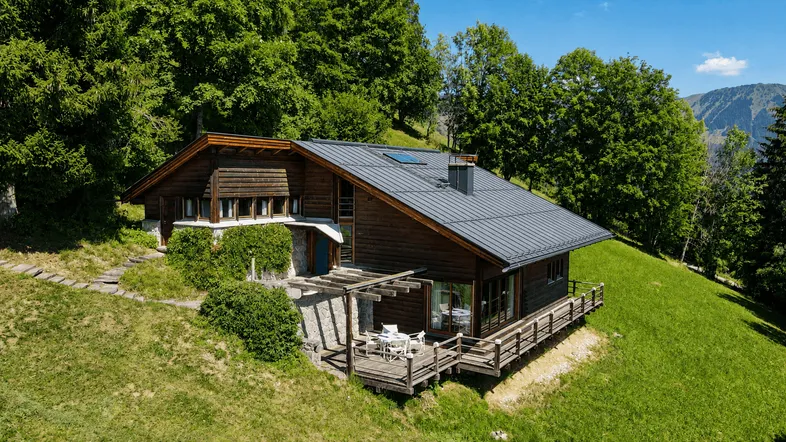 Modernes Holzhaus mit Satteldach und Terrasse, umgeben von grünen Bäumen und Wiesen.