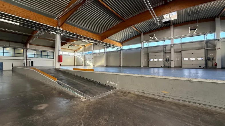 Geräumige Lagerhalle mit Laderampe, hohen Decken, Holzträgern und Rolltoren für einfachen Zugang.