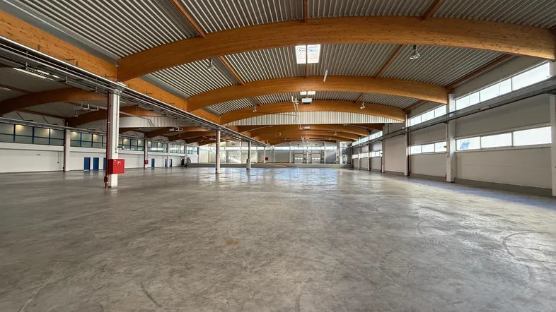 Geräumige, leere Lagerhalle mit hohen Decken, Holzbalken und viel Tageslicht durch Oberlichter.