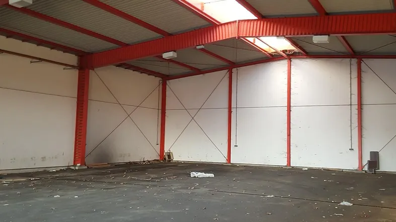 Große, leere Lagerhalle mit roter Stahlkonstruktion, Wellblechdach und Oberlichtern für Tageslicht.
