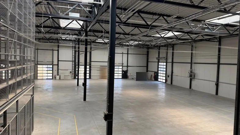 Weitläufige Lagerhalle mit hohen Decken, Betonboden und sichtbaren Metallregalen an der Seite.