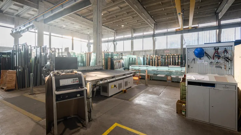Geräumige Industriehalle mit hohen Decken, Betonpfeilern und spezialisierten Glasbearbeitungsmaschinen.