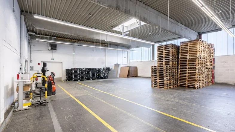 Große Lagerhalle mit hohen Decken, Betonboden und gestapelten Paletten, bereit zur Nutzung.