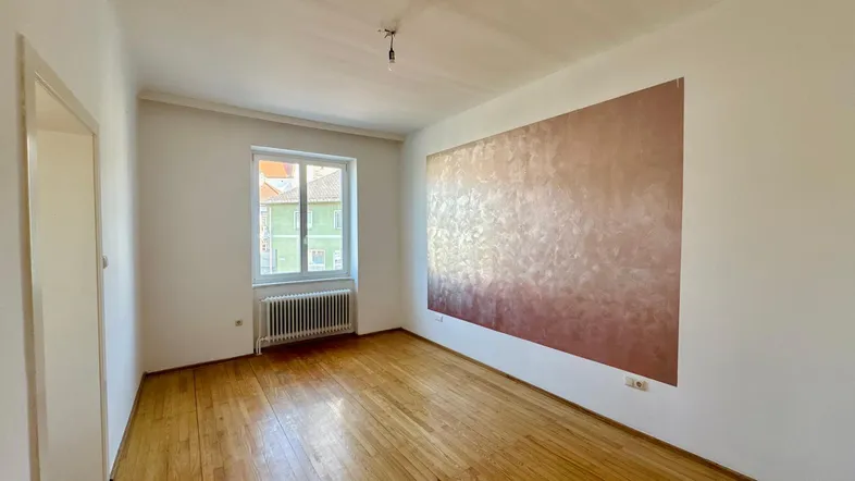 Helles Zimmer mit Holzboden, einer Akzentwand und Blick nach draußen durch das Fenster.