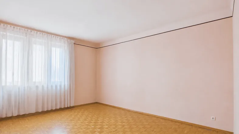 Helles, leeres Zimmer mit Fischgrätparkettboden und großen Fenstern, bereit zur individuellen Gestaltung.