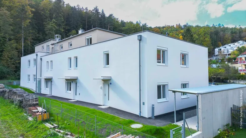 Modernes Mehrfamilienhaus mit weißer Fassade und grüner Umgebung am Waldrand.