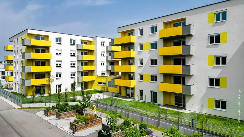 Moderne Wohngebäude mit leuchtend gelben Balkonen und gepflegten Außenanlagen.