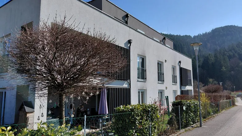 Moderne Wohnanlage mit heller Fassade, kleinem Vorgarten und Bergblick im Hintergrund.