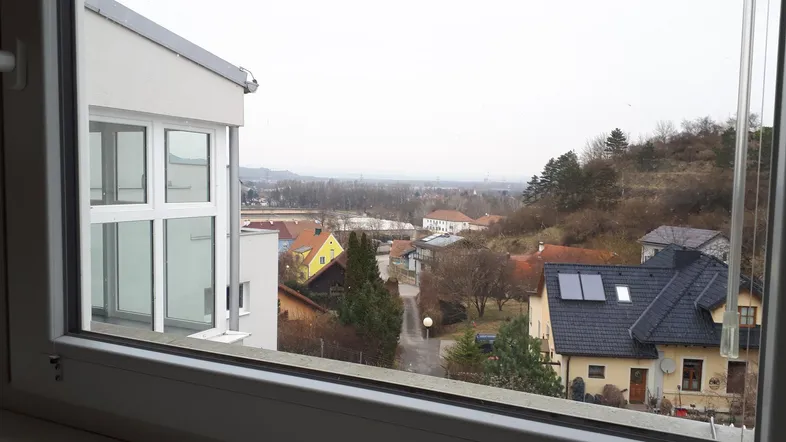 Blick aus einem Fenster auf eine ländliche Umgebung mit Häusern und Bäumen unter bewölktem Himmel.