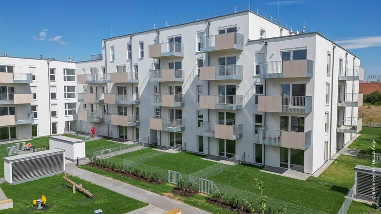 Moderne Wohnanlage mit weißen Fassaden, Balkonen und einem grünen Innenhof mit Spielplatz.