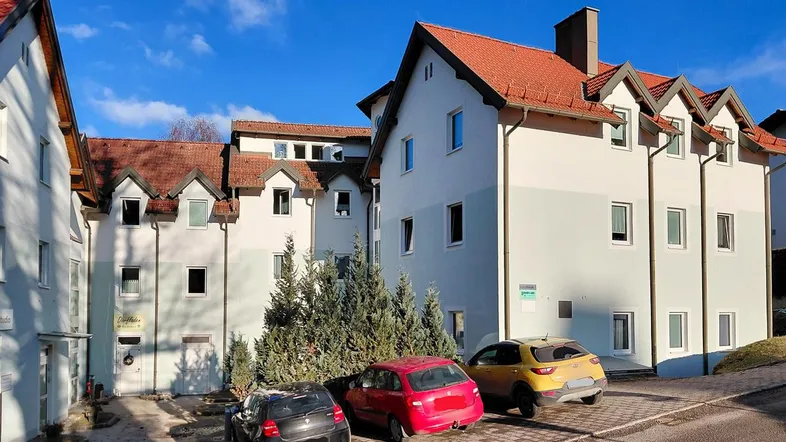 Mehrere Wohngebäude mit Satteldächern und Parkplätzen unter blauem Himmel in einer ländlichen Umgebung.
