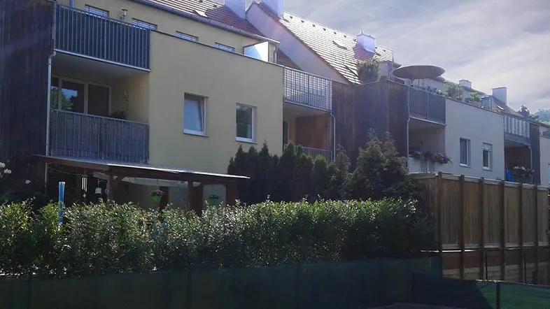 Modernes Mehrfamilienhaus mit mehreren Balkonen und begrüntem Vorgartenbereich.