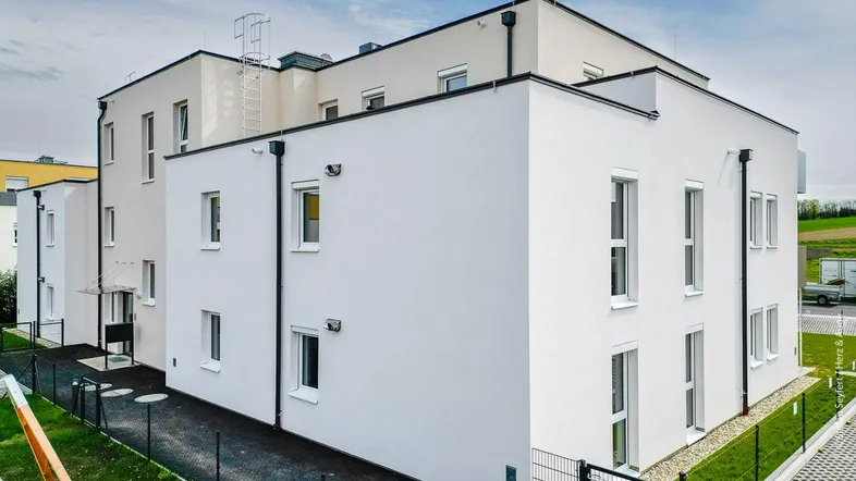 Modernes Mehrfamilienhaus mit weißer Fassade und vielen Fenstern unter blauem Himmel.